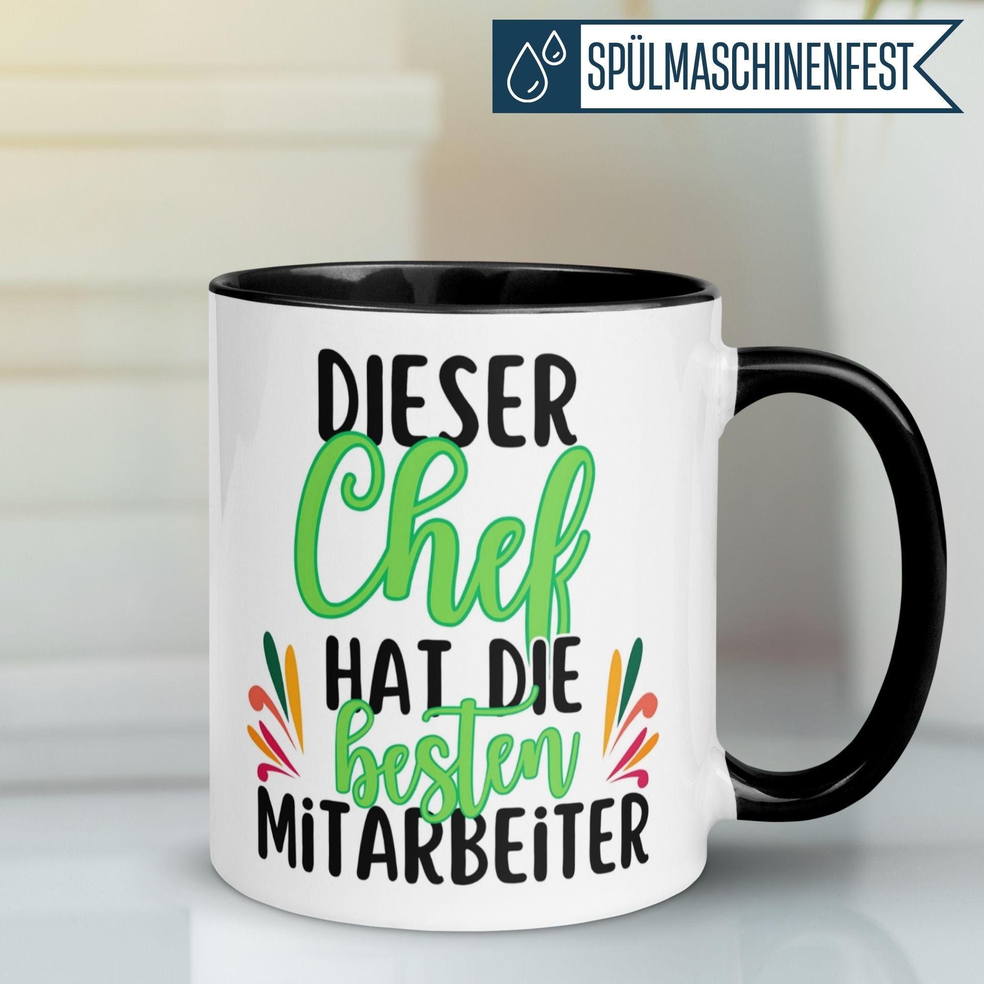 Momentals Tasse mit Spruch „Dieser Chef hat die besten Mitarbeiter“ in bunten Farben auf schwarzem Hintergrund.