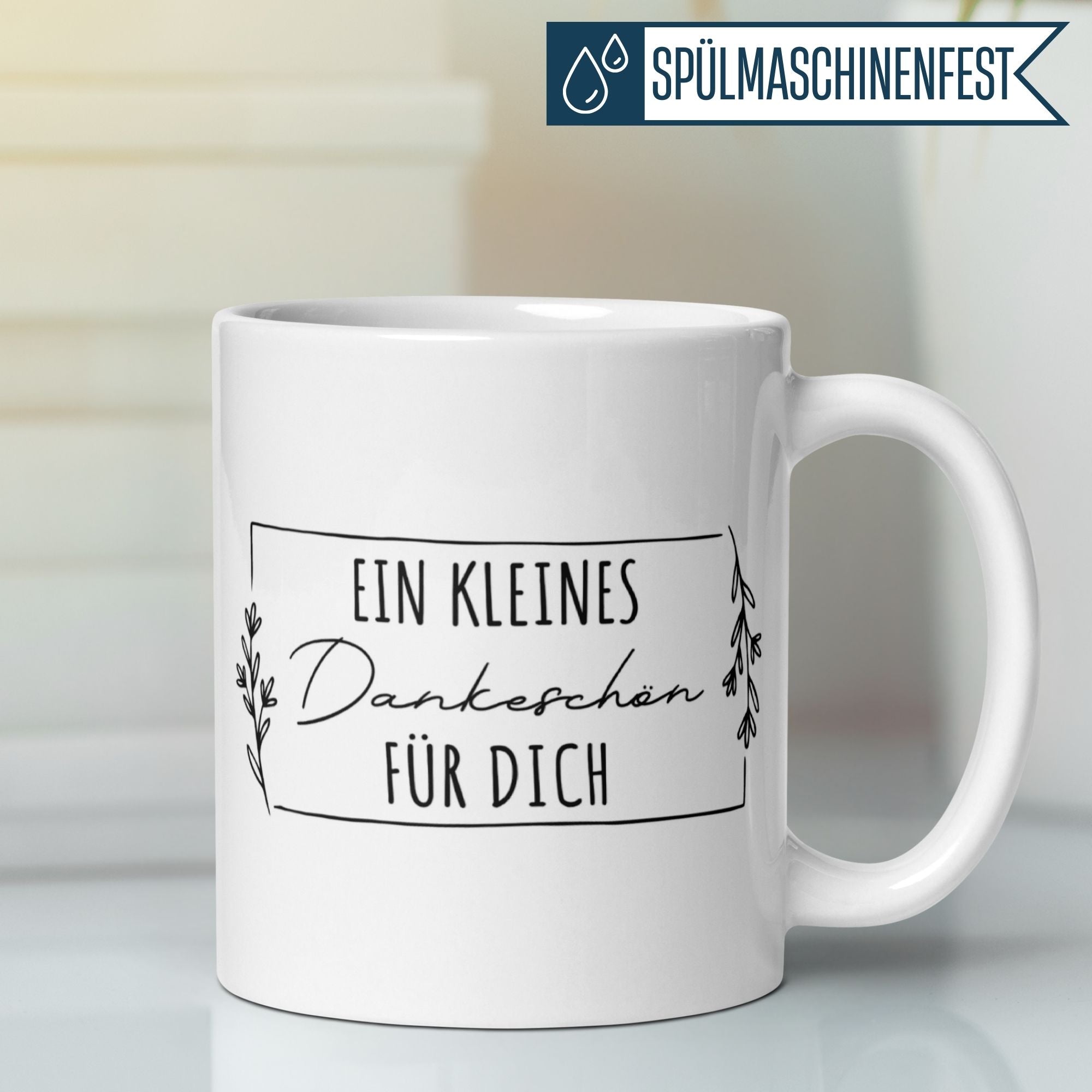 Weißer Kaffeebecher mit dem Schriftzug "Ein kleines Dankeschön für dich" und zarten Blättern.