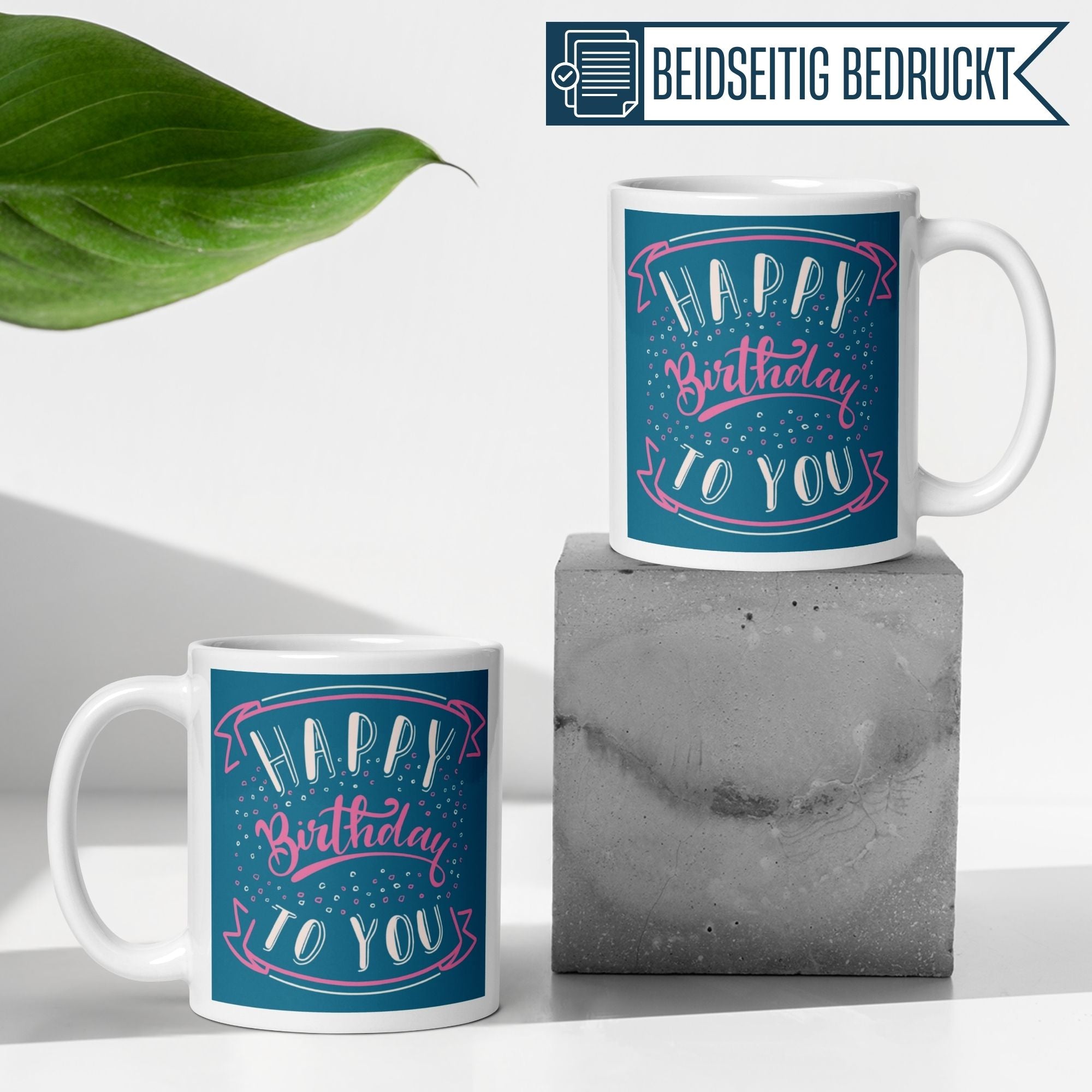 Zwei Momentals® Tassen mit buntem "Happy Birthday to You" Design auf einem grauen Untergrund.
