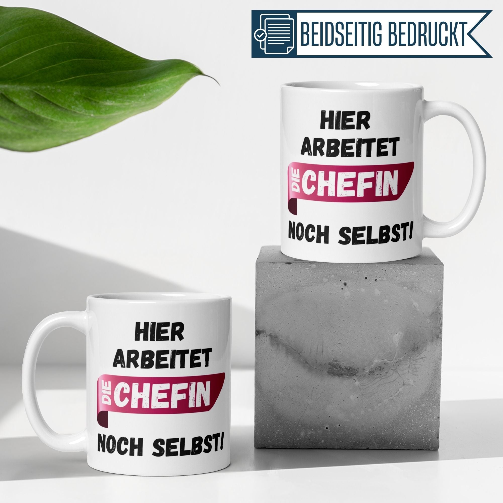 Momentals Tasse Chefin mit Spruch "Hier arbeitet die Chefin noch selbst!" auf grauem Untergrund.