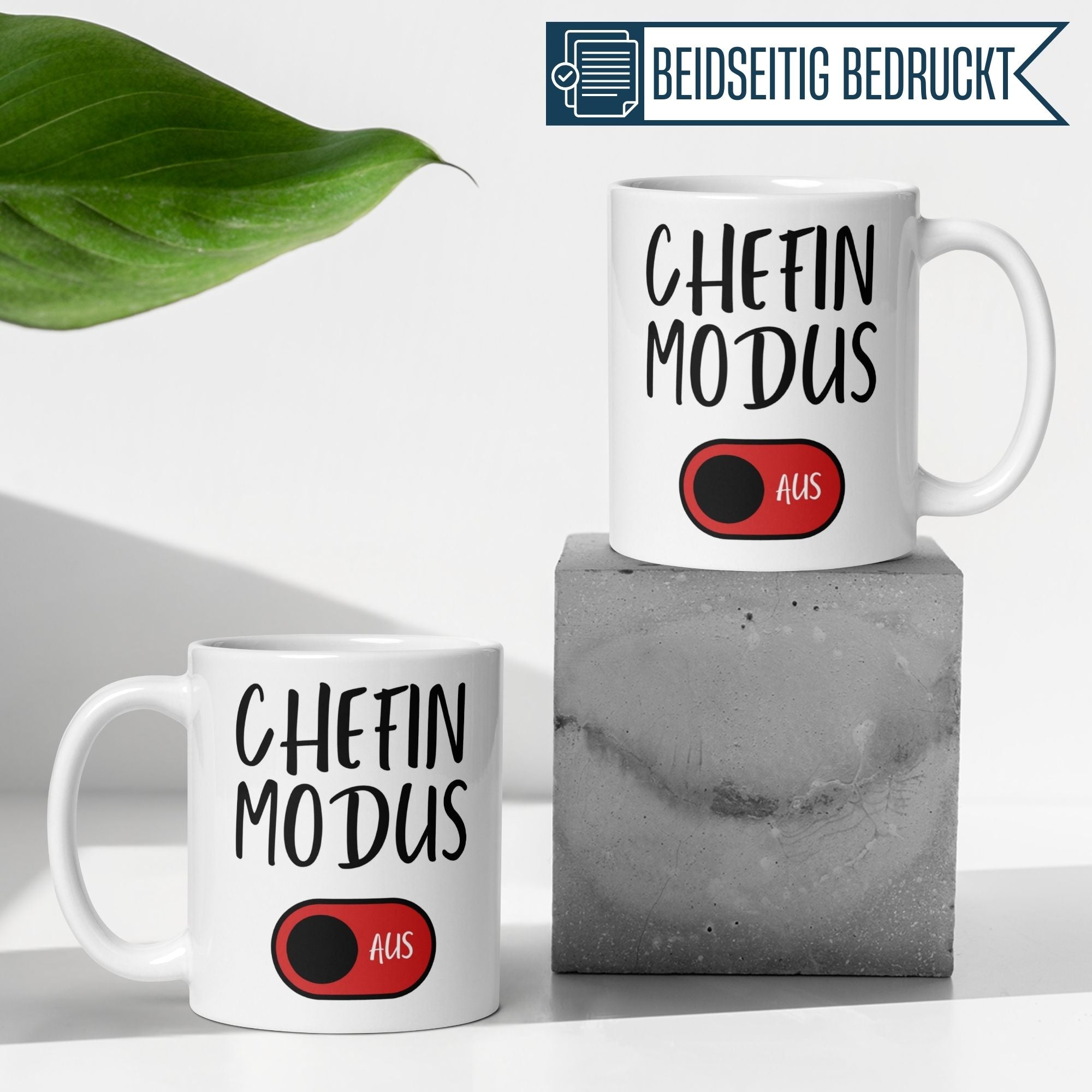 Zwei Momentals Tassen mit "Chefin Modus AUS" und rotem Schalter auf einem grauen Block, perfekt für Abschiedsgeschenke.