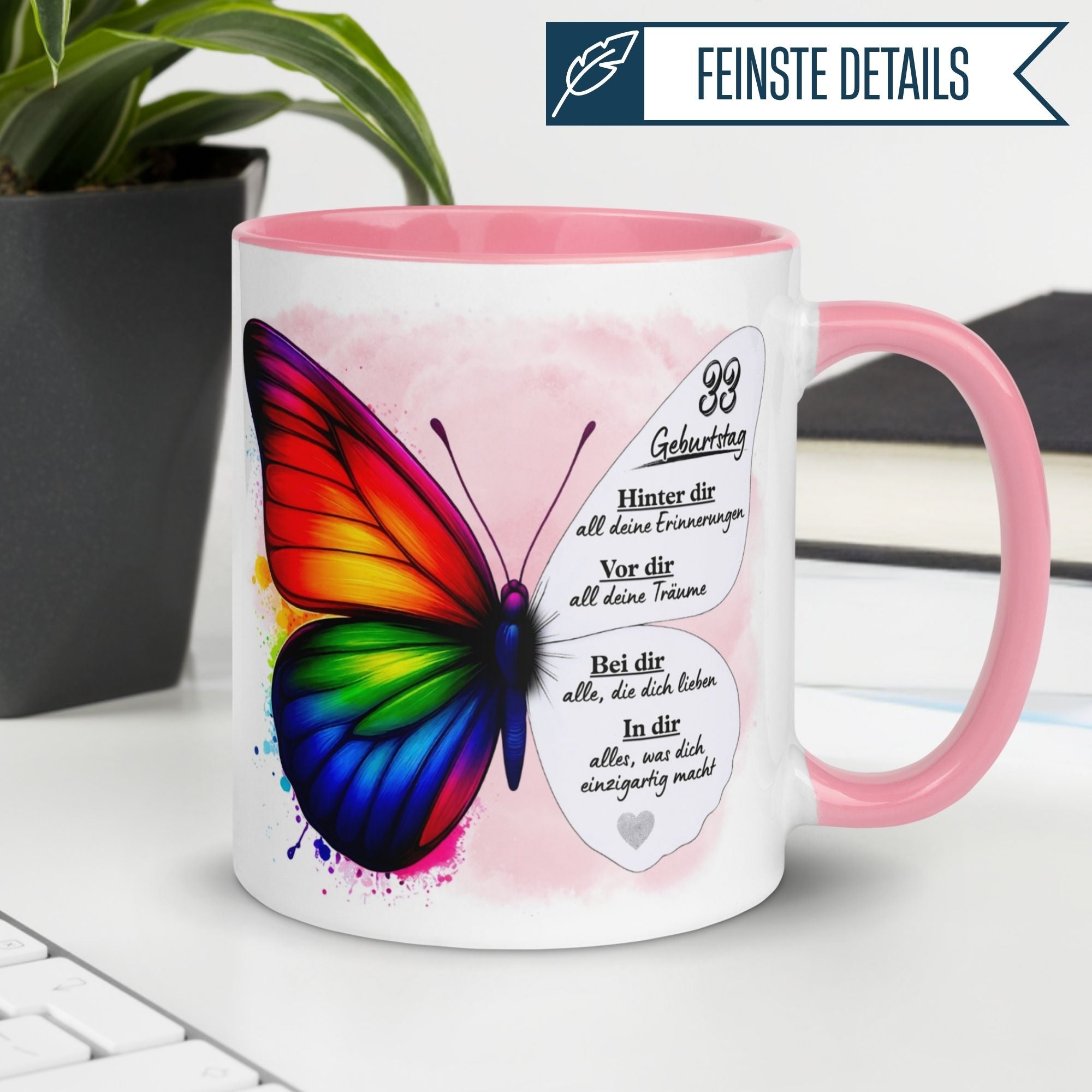Momentals® Tasse zum 33. Geburtstag mit buntem Schmetterling und inspirierendem Spruch auf einem Tisch.