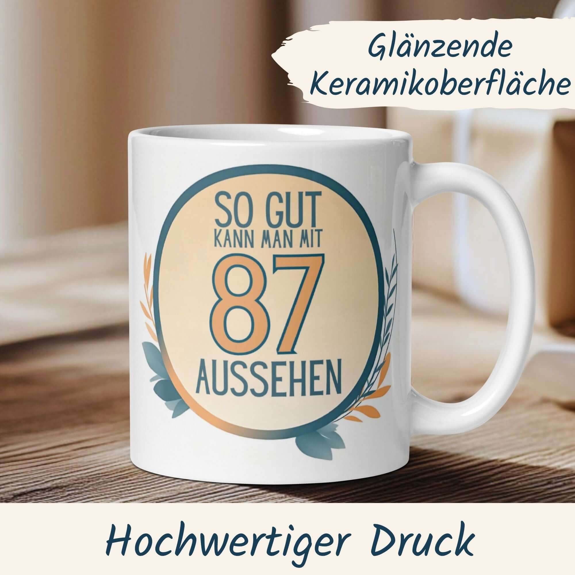 Tasse zum 87. Geburtstag mit humorvollem Spruch "So gut kann man mit 87 aussehen" und stilvollem Blätterkranz.