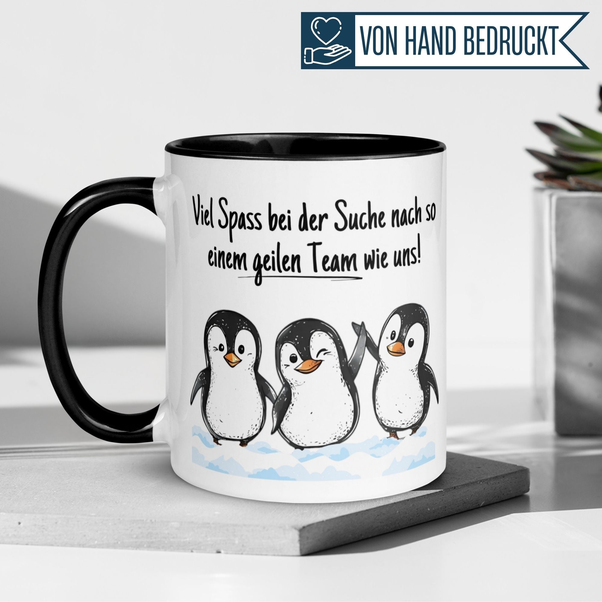 Schwarze Tasse mit Pinguinen und Spruch: 'Viel Spaß bei der Suche nach so einem geilen Team wie uns!'.
