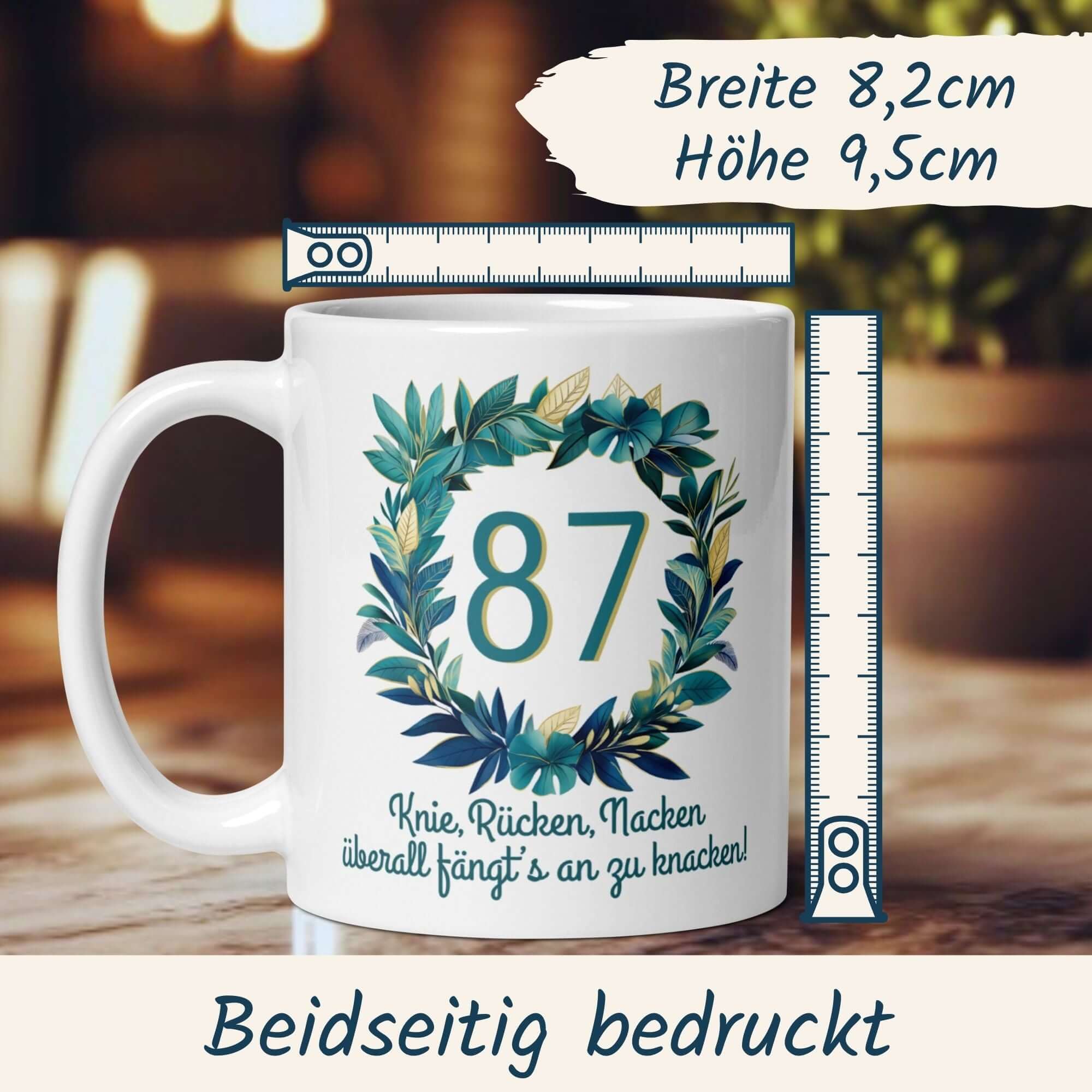 Witzige Tasse zum 87. Geburtstag mit Blumenkranz und Spruch "Knie, Rücken, Nacken – überall fängt’s an zu knacken!"