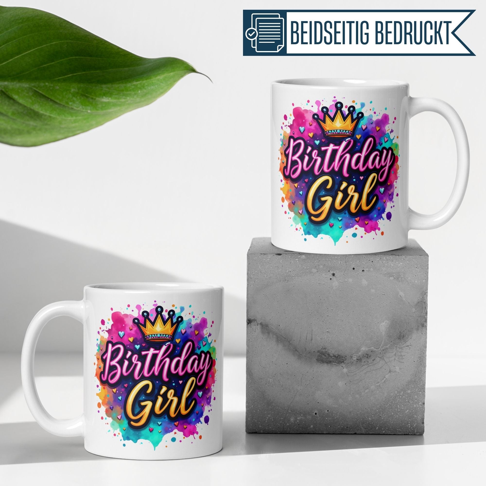 Bunte Tasse für das Geburtstagskind mit Krone und Herzchen auf einem Betonsockel.