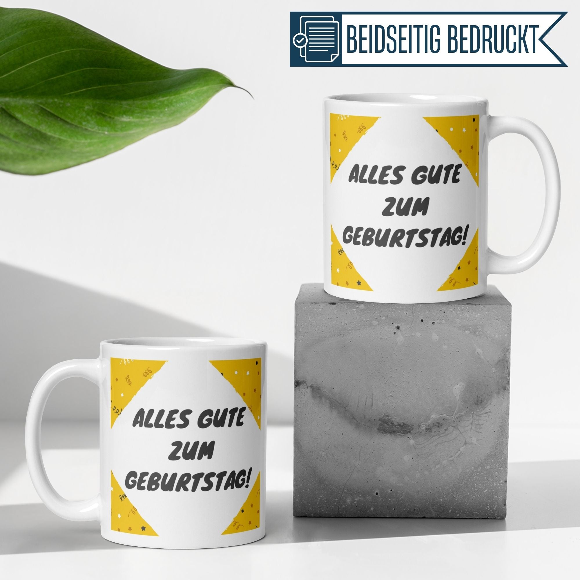Zwei bunte Geburtstagstassen mit dem Spruch 'Alles Gute zum Geburtstag!' auf einem modernen Betonblock.
