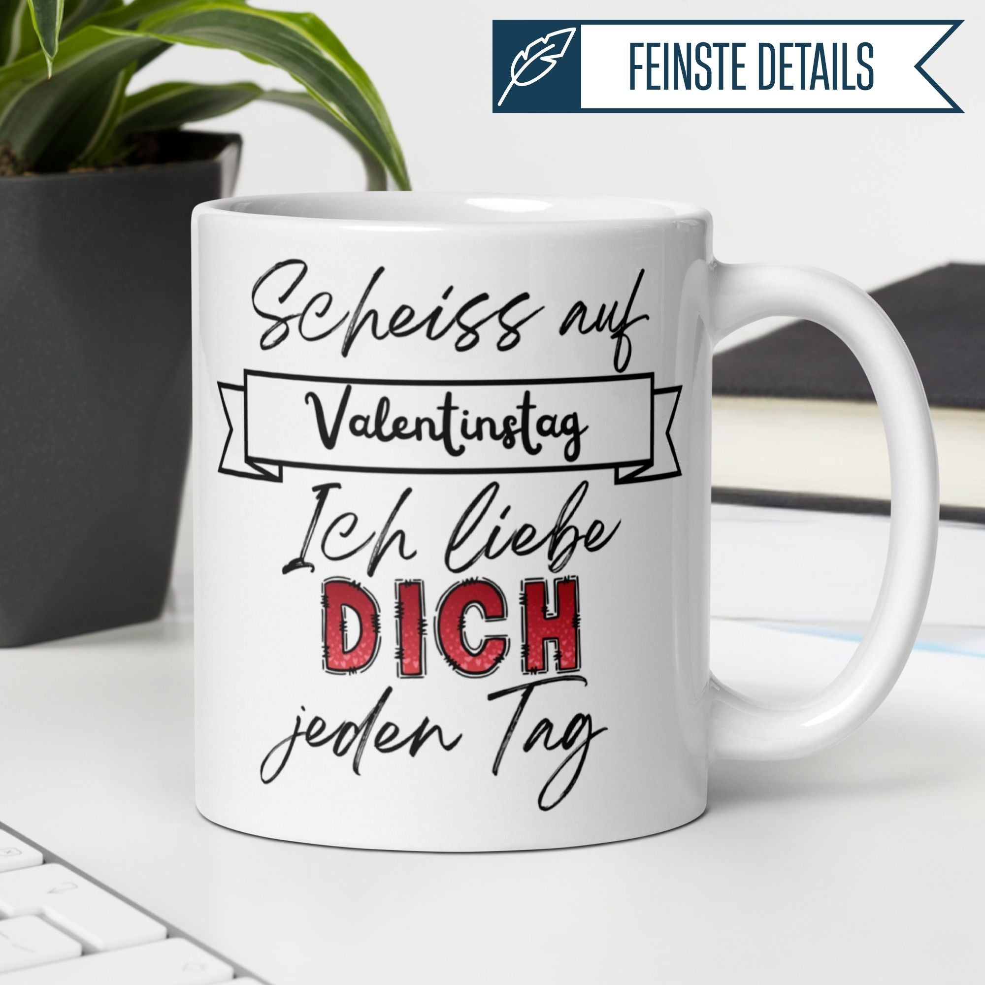Weiße Tasse mit Spruch "Scheiss auf Valentinstag – Ich liebe Dich jeden Tag" auf einem Schreibtisch.