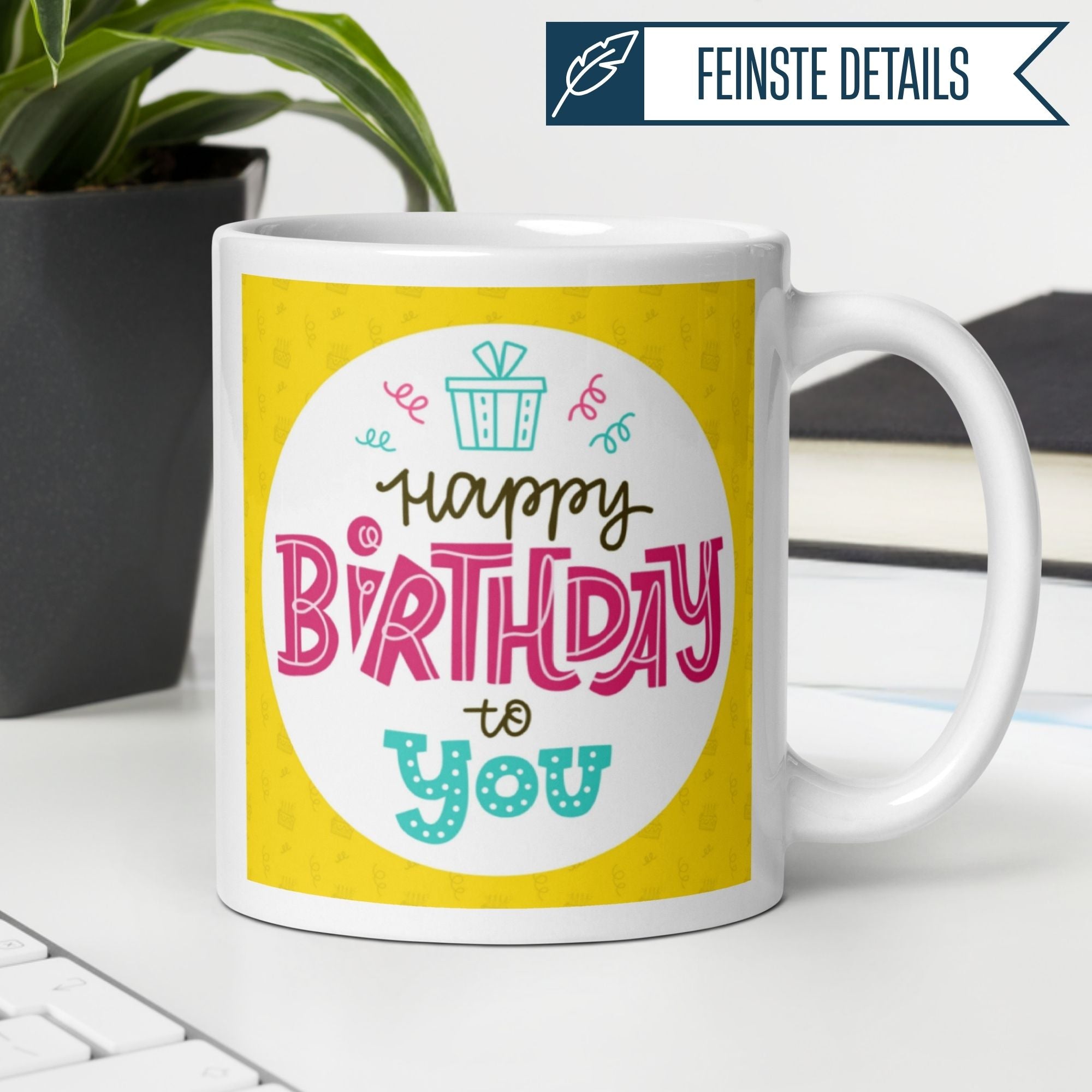 Bunte Geburtstagstasse mit dem Schriftzug "Happy Birthday to you" auf gelbem Hintergrund.