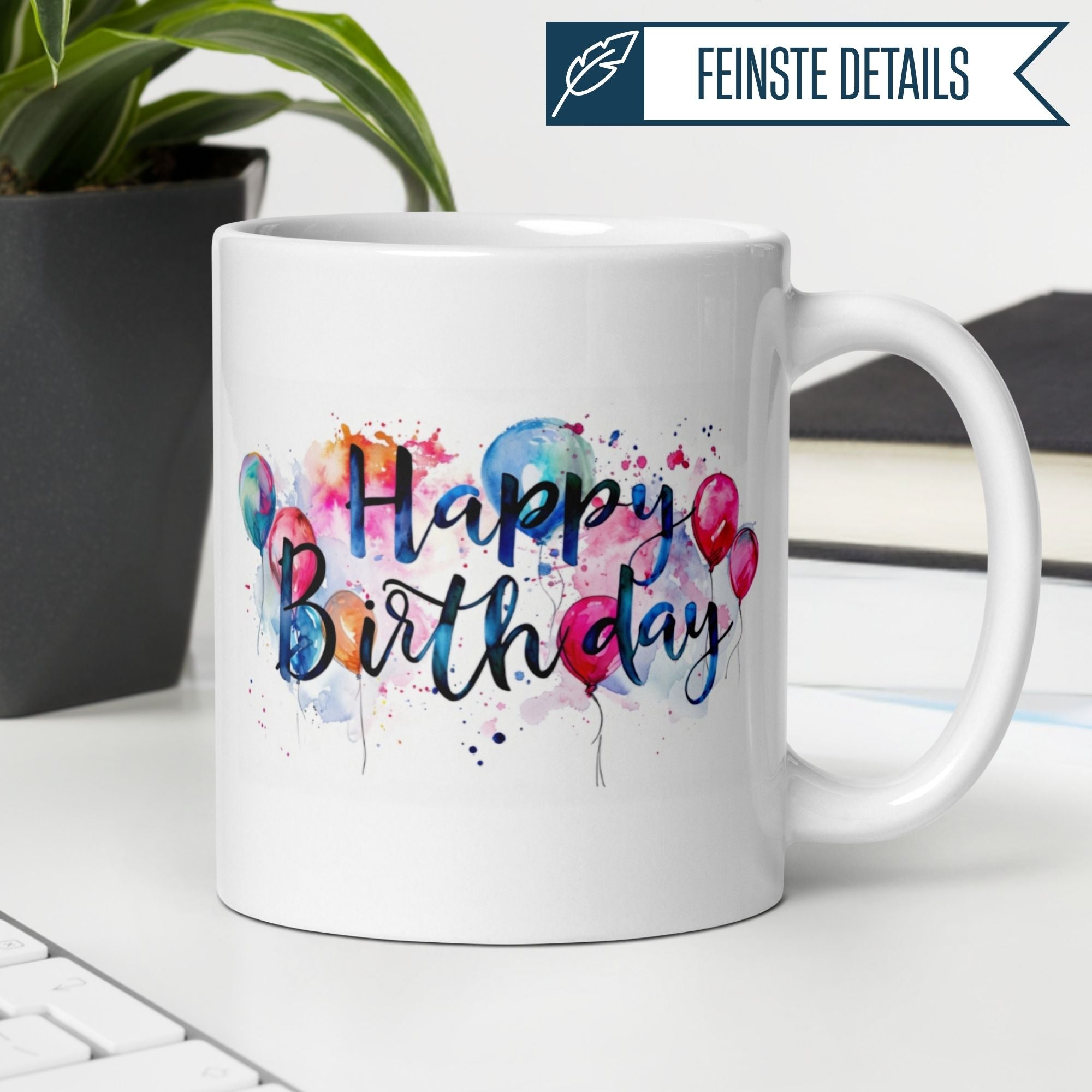 Farbige Aquarell-Tasse mit "Happy Birthday" Design und Ballons auf einem Schreibtisch.