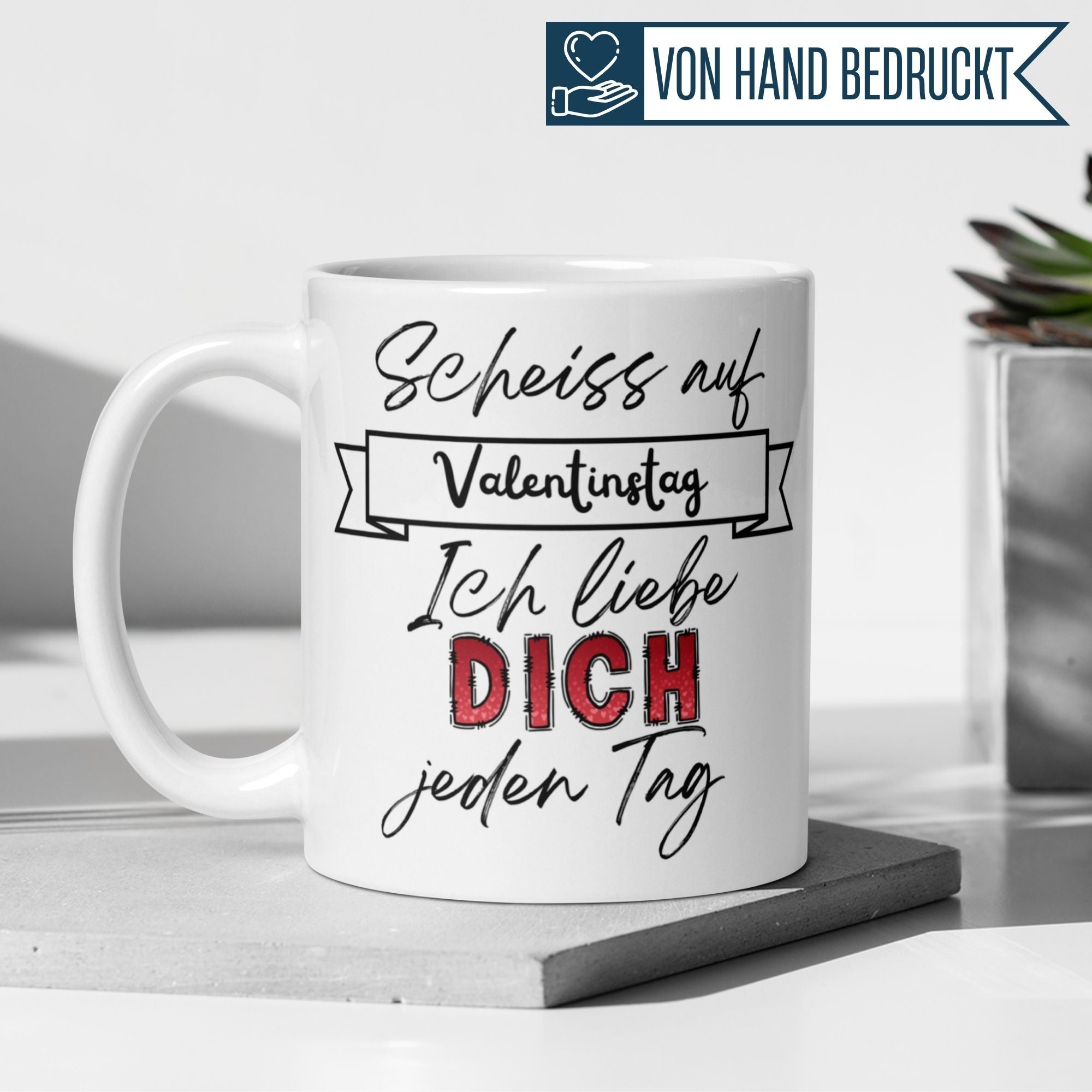 Weiße Tasse mit dem Spruch „Scheiss auf Valentinstag – Ich liebe Dich jeden Tag“ auf einem Tisch.