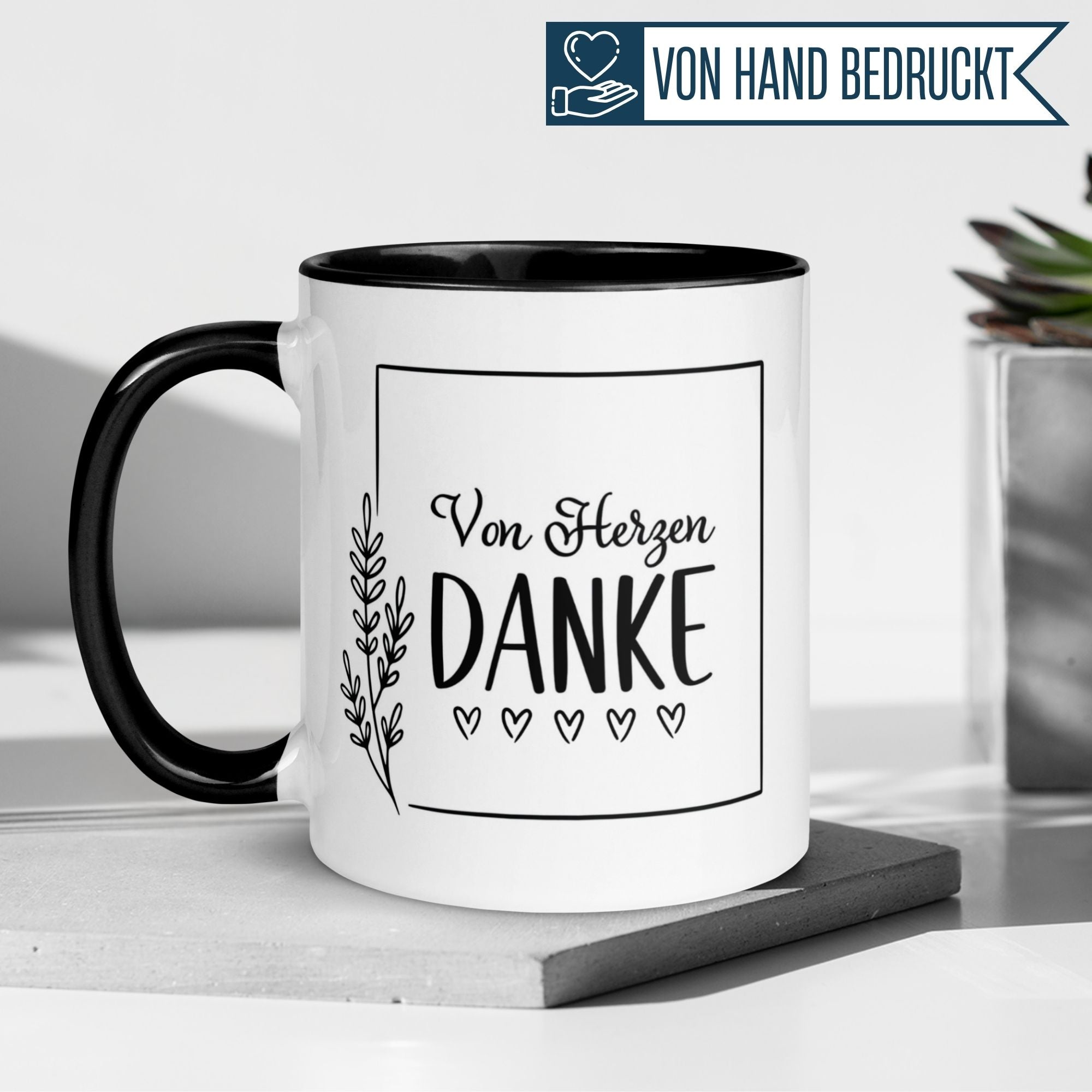 Momentals Tasse 'Von Herzen Danke' mit floralem Design, schwarz-weiße Keramiktasse auf Tisch.
