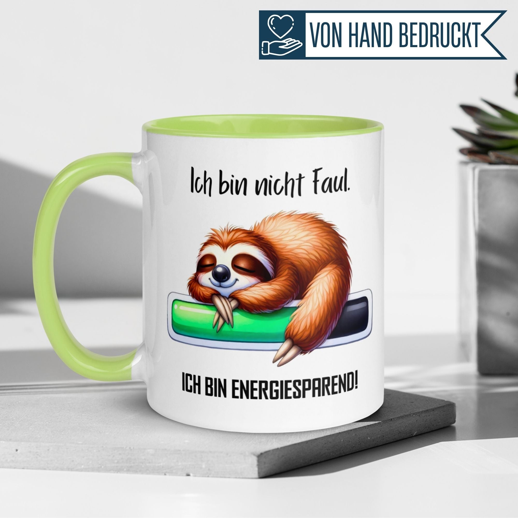 Momentals Tasse mit faultier und Spruch "Ich bin nicht faul - ich bin energiesparend!" auf grünem Hintergrund.