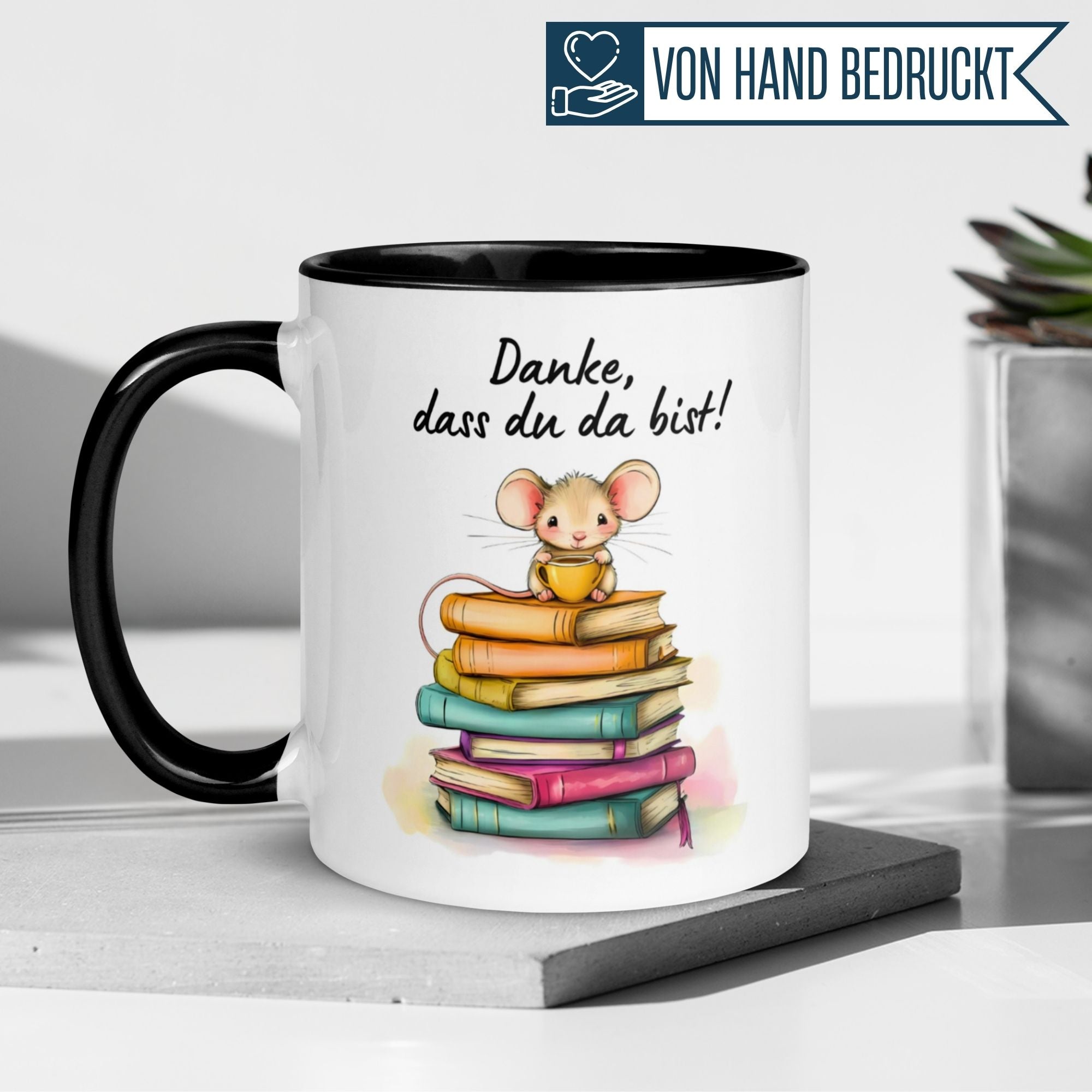 Momentals Tasse mit Mäuse-Motiv und der Aufschrift 'Danke, dass du da bist!' auf Bücherstapeln.