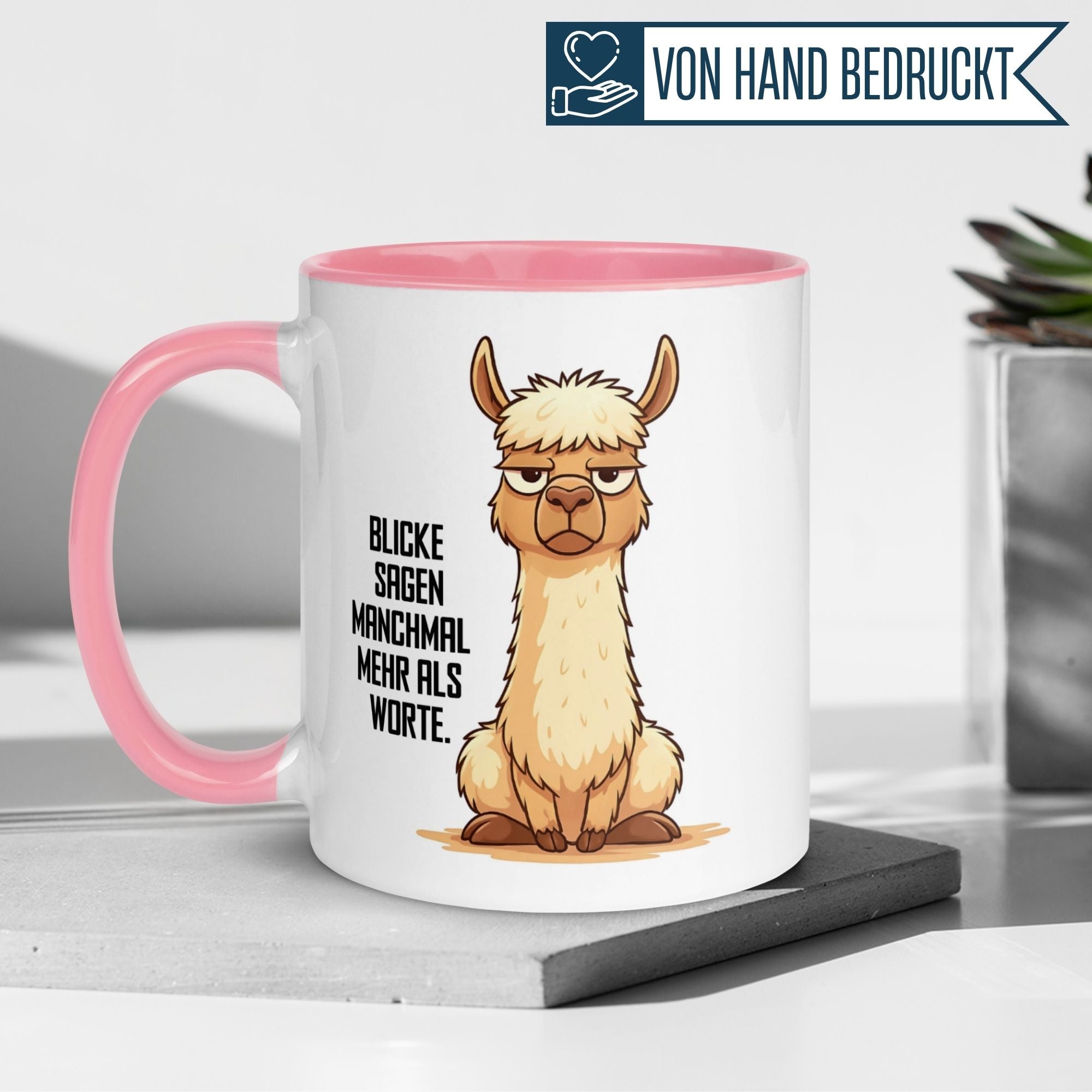 Momentals Tasse mit mies gelauntem Lama und Spruch: 'Blicke sagen manchmal mehr als Worte.' Auf rosa Hintergrund.