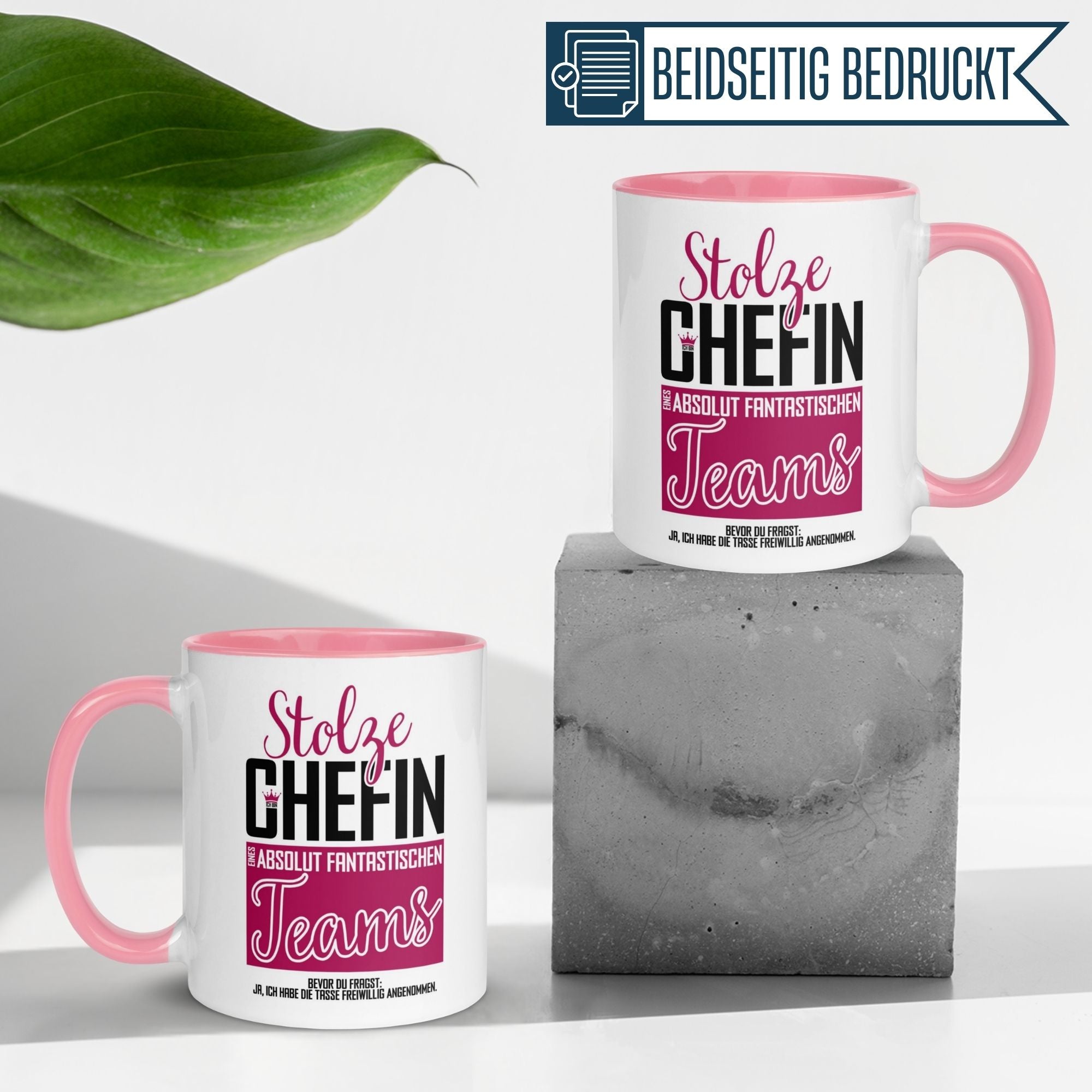 Zwei pink akzentuierte Tassen mit dem Spruch "Stolze Chefin eines absolut fantastischen Teams" auf einer Betonbasis.