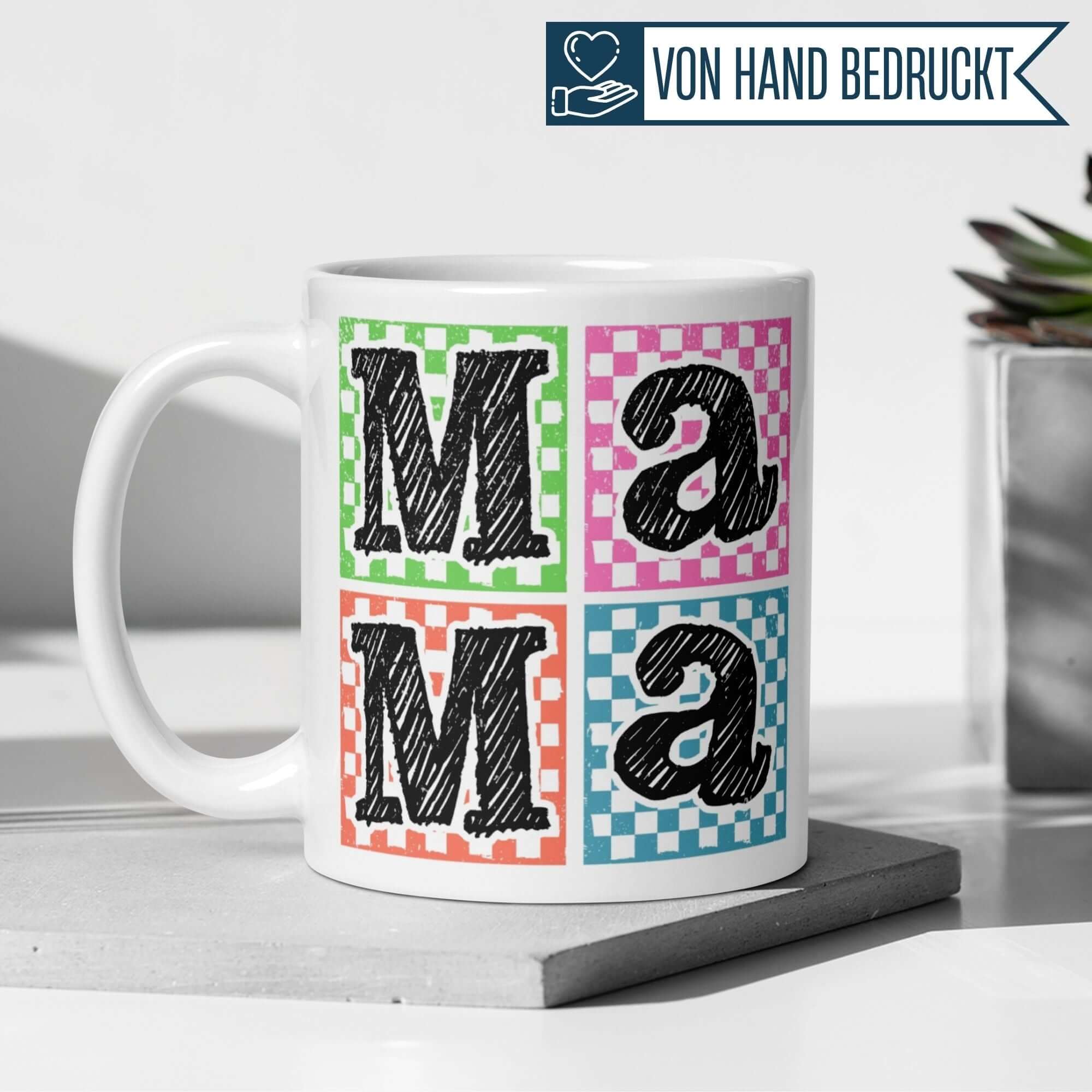 Bunte Mama Tasse mit Schraffur-Design und Karomuster in Grün, Pink, Orange und Blau auf einem Tisch.